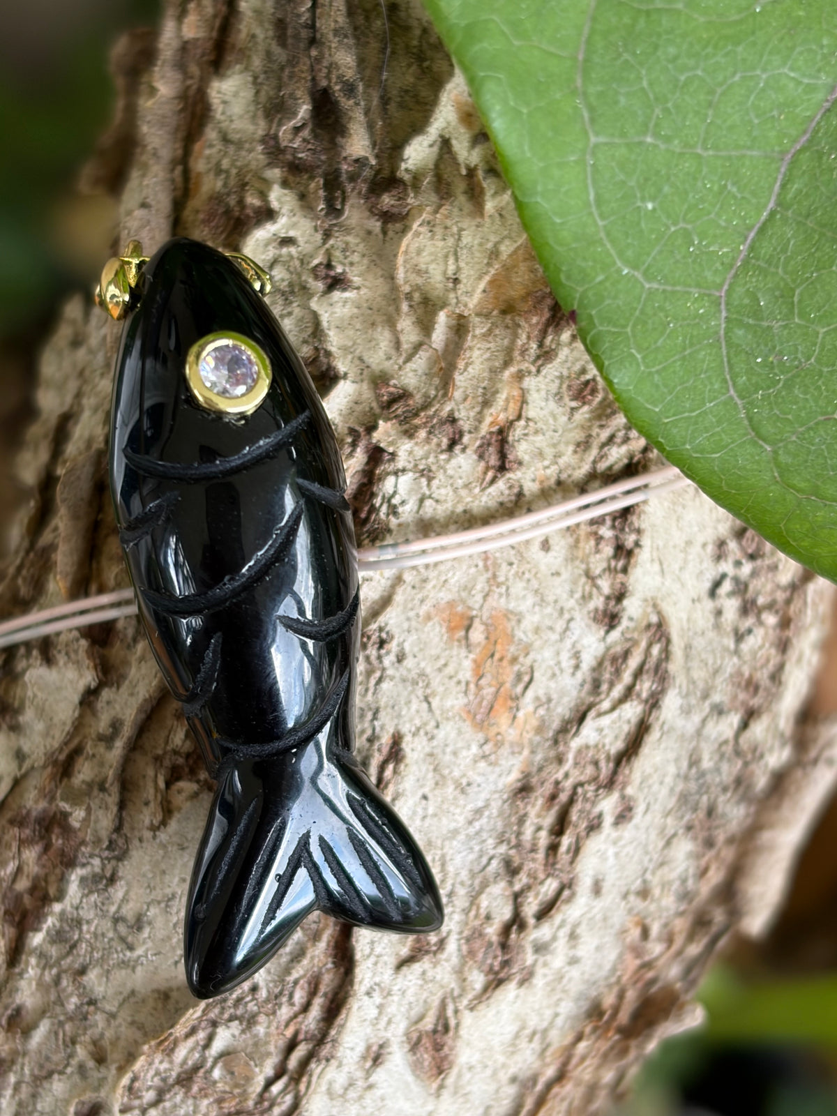 Hand-carved black gemstone fish charm with crystal eye and gold-tone bail on driftwood
