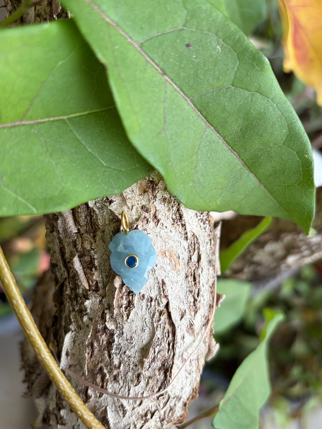 Hand-carved pale blue gemstone flower charm with deep blue center stone and gold-tone bail on driftwood