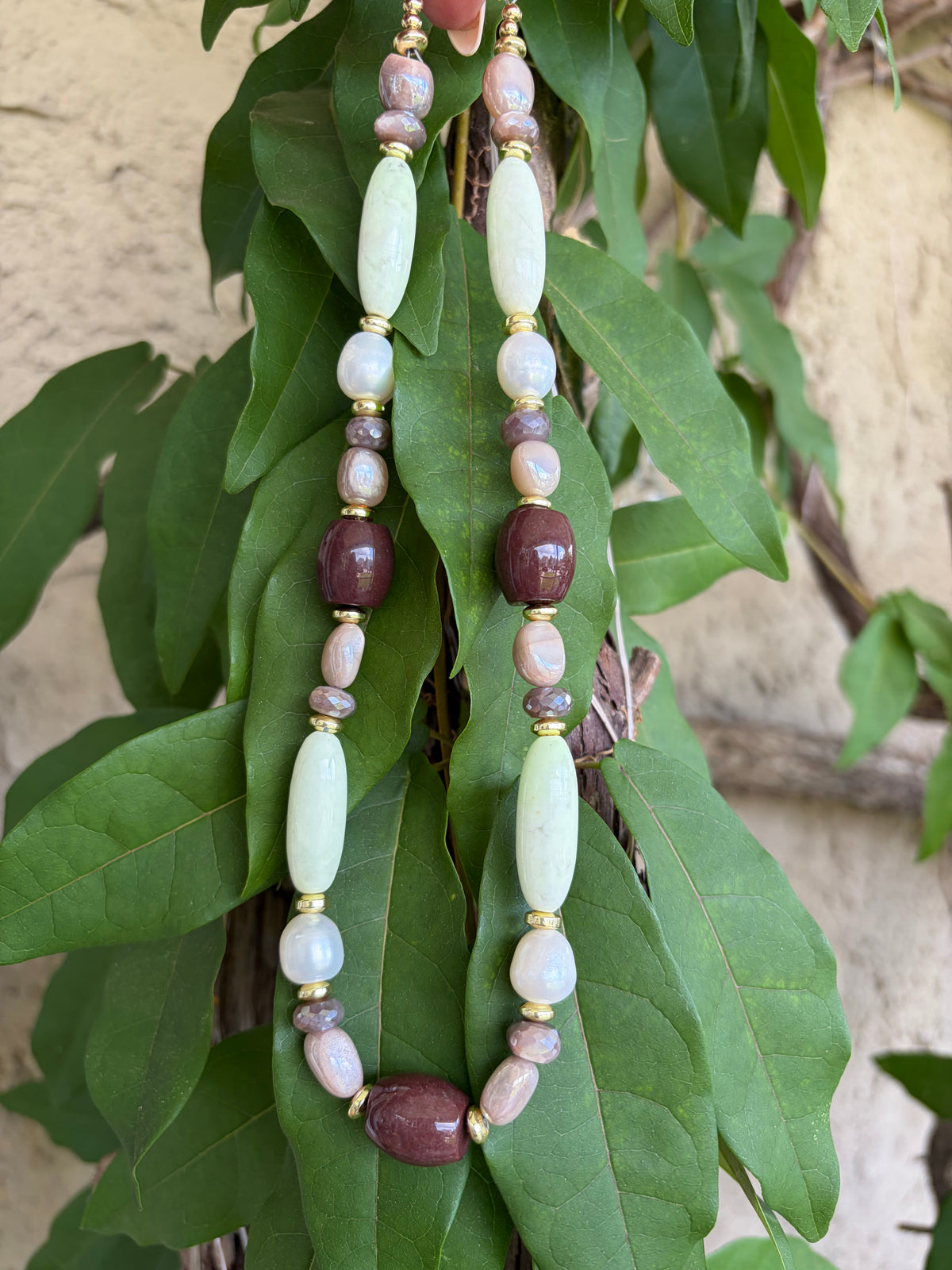 Mixed stone necklace draped over green leaves showing clasp