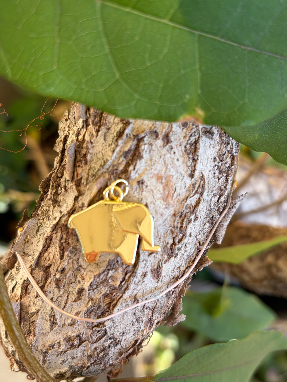 Gold origami elephant charm with jump ring bail on tree bark