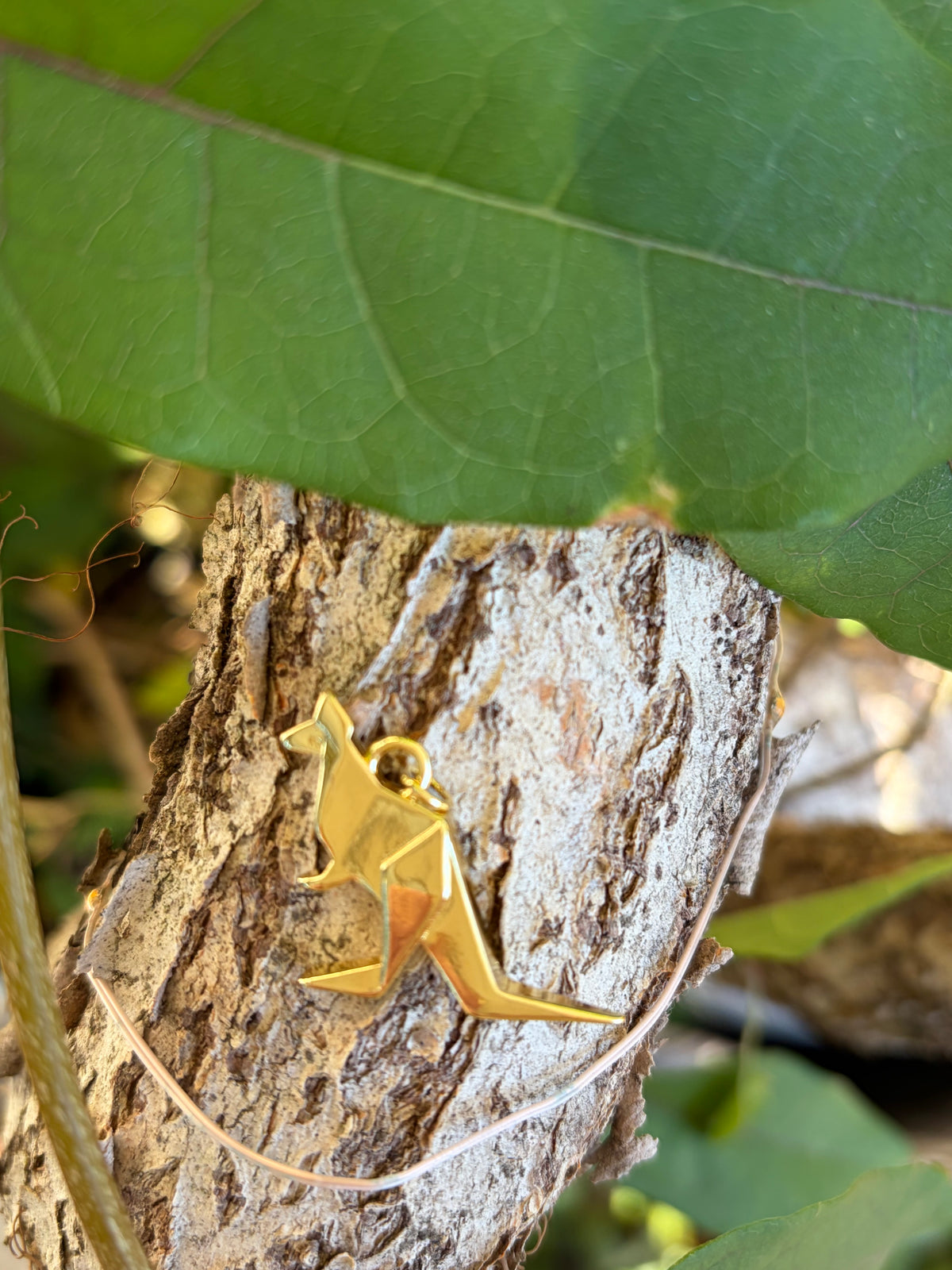Gold origami kangaroo charm with jump ring bail on tree bark
