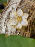 White pearlescent enamel five-petal flower charm with gold border and bead center on tree bark