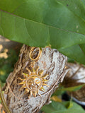 Gold sun face charm with radiating rays hanging from gold clasp on tree bark