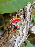 Colorful toucan enamel charm with gold compass rose on tree bark