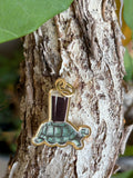 Guinness Turtle enamel charm with gold-tone border hanging on tree bark