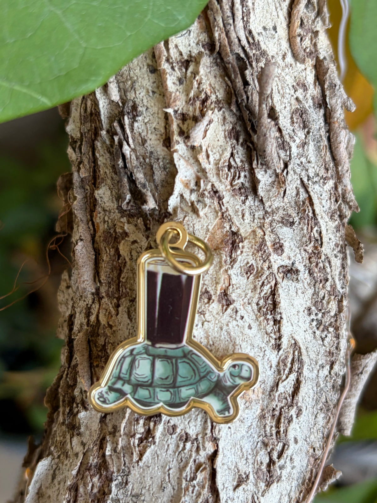 Guinness Turtle enamel charm with gold-tone border hanging on tree bark