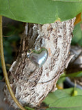 Silver puff heart charm with bail on tree bark with green leaves