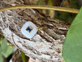White enamel cushion square charm with navy blue center stone on tree bark
