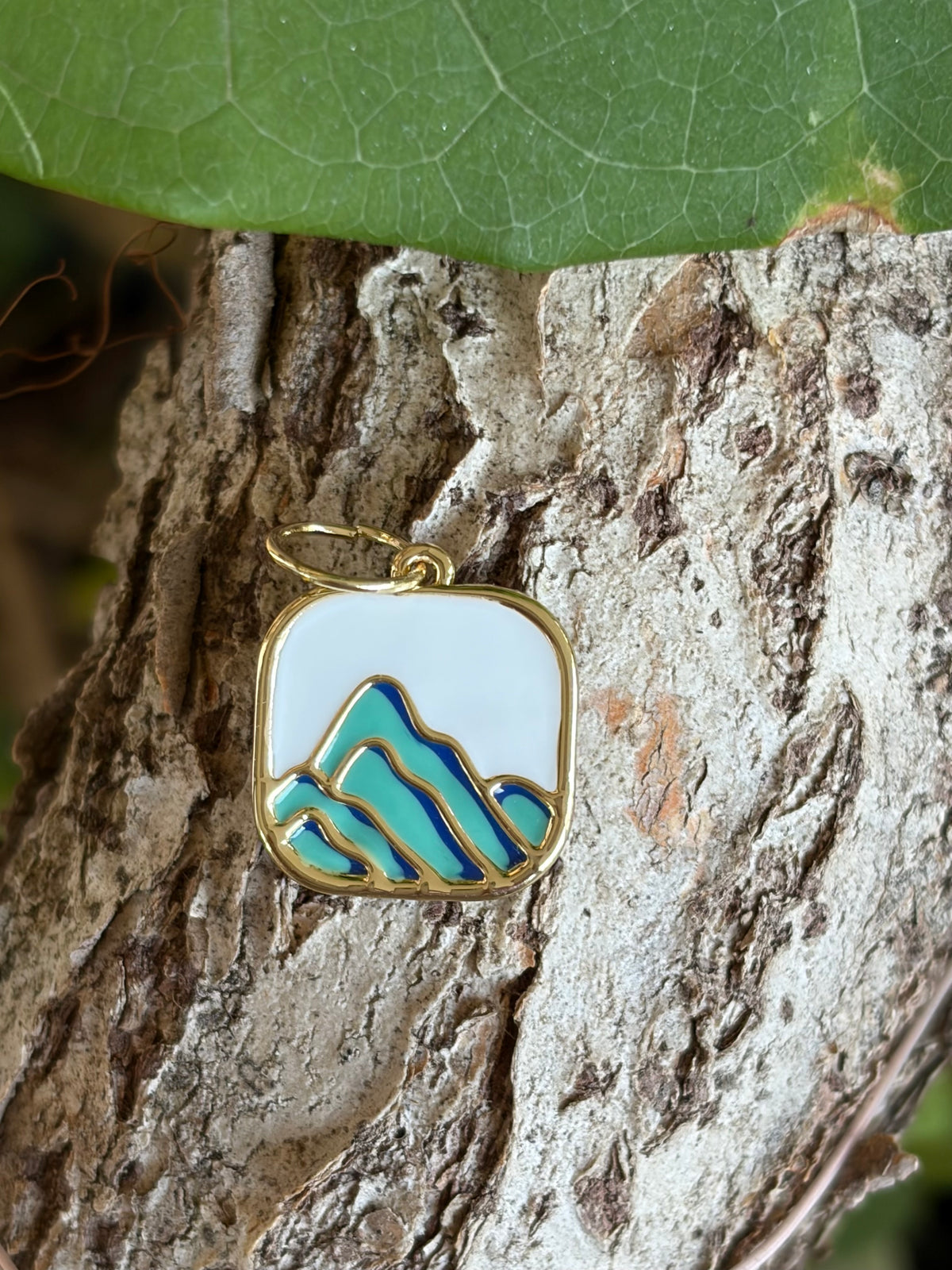 Square gold-tone enamel charm with teal and blue mountain landscape on tree bark