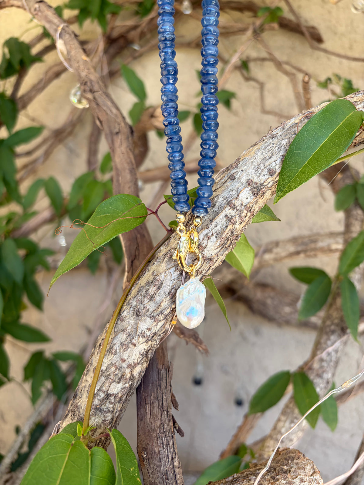 Kyanite heishi necklace with baroque pearl pendant draped on leaves