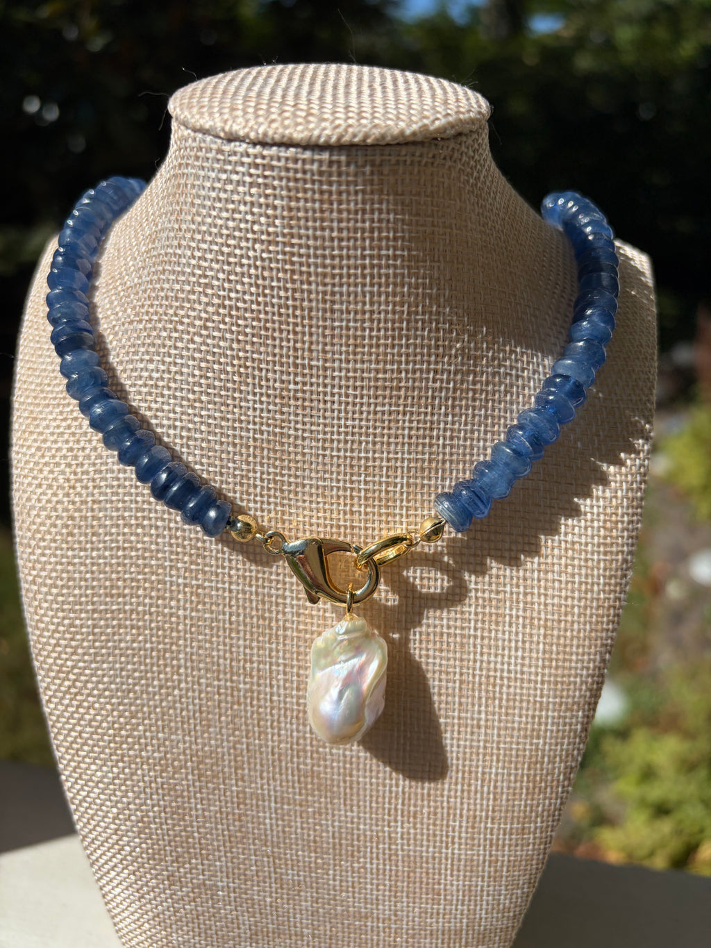 Kyanite heishi necklace with baroque pearl pendant on large green leaves