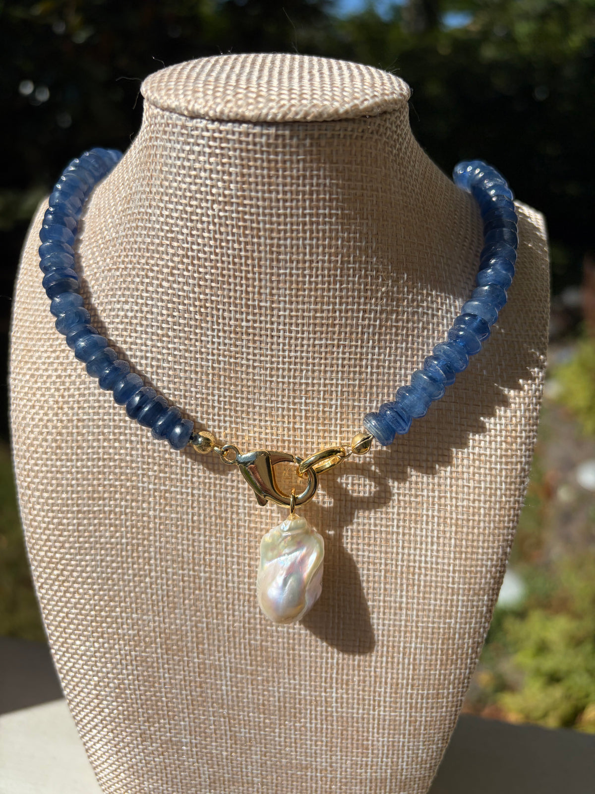 Kyanite heishi necklace with baroque pearl pendant on large green leaves