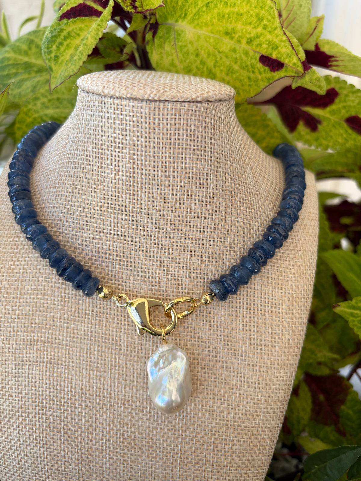 Kyanite heishi necklace with baroque pearl pendant on branch with leaves