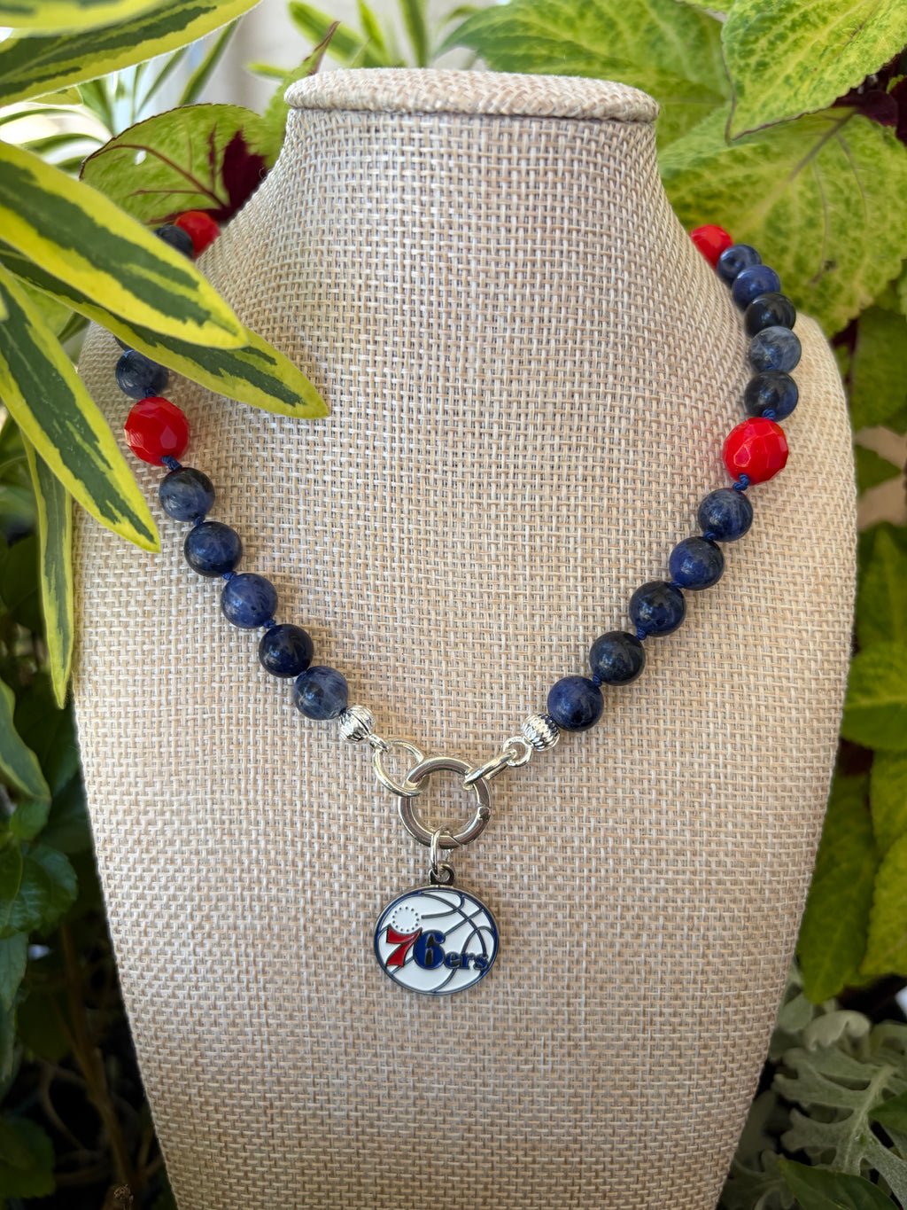 Sodalite and coral necklace with 76ers charm on mannequin bust with colorful foliage