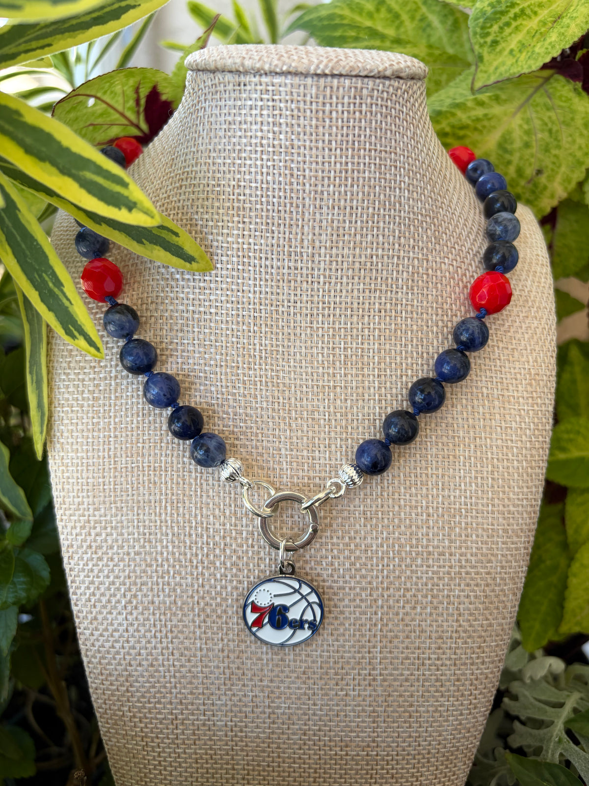 Sodalite and coral necklace with 76ers charm on mannequin bust with colorful foliage