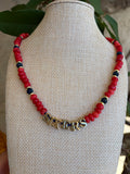 Red rondelle and navy crystal SIXERS necklace draped on green leaves