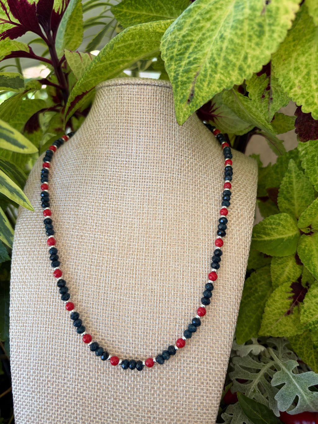 Navy crystal and red bead necklace draped on green leaves