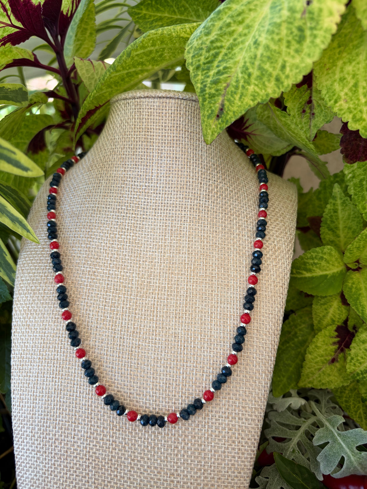 Navy crystal and red bead necklace draped on green leaves