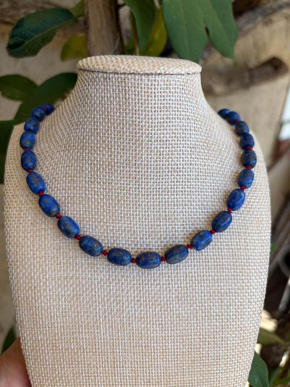 Lapis lazuli beaded necklace with gold toggle clasp draped on leaves and driftwood