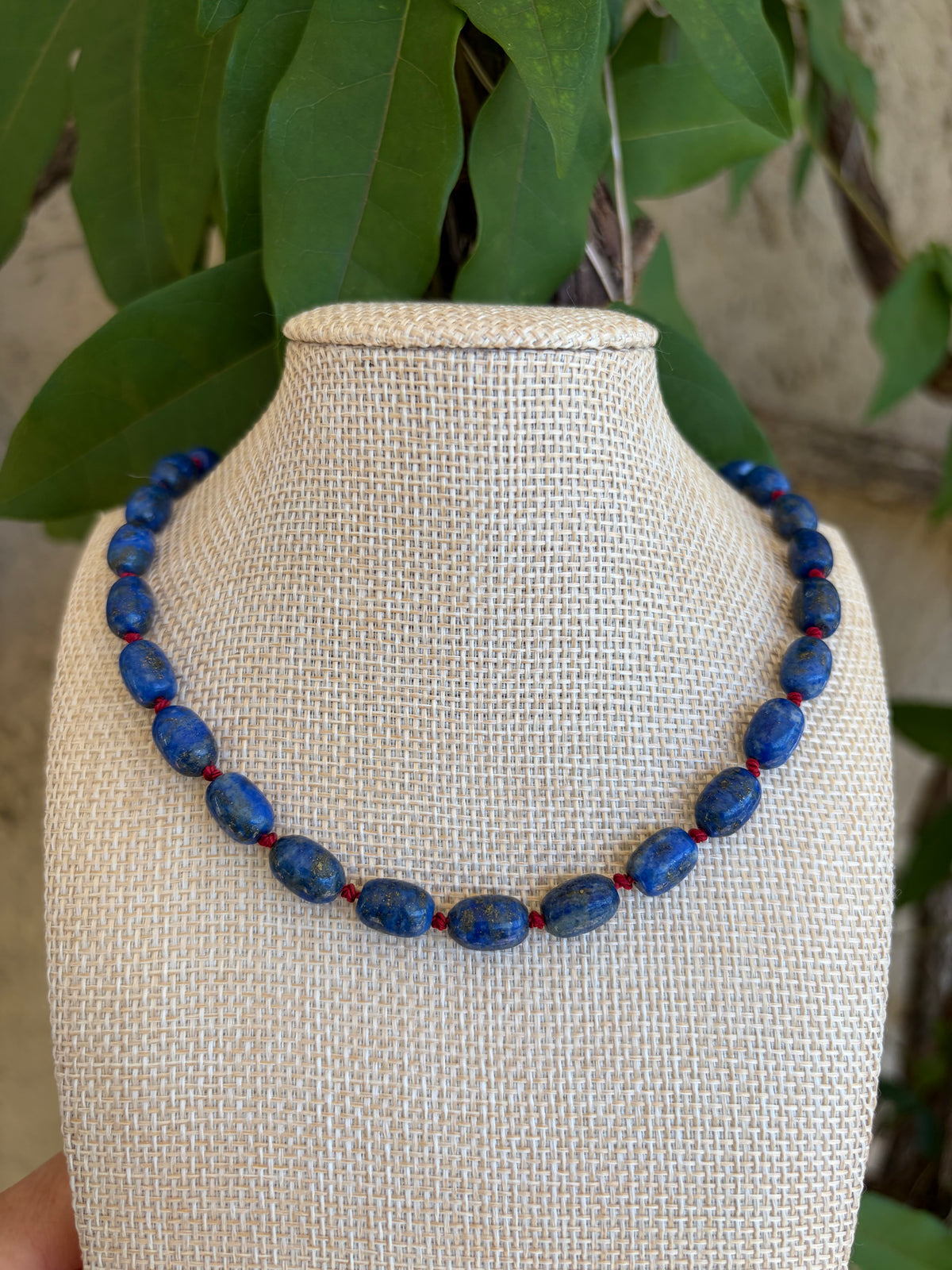 Lapis lazuli beaded necklace with gold toggle clasp on green leaves