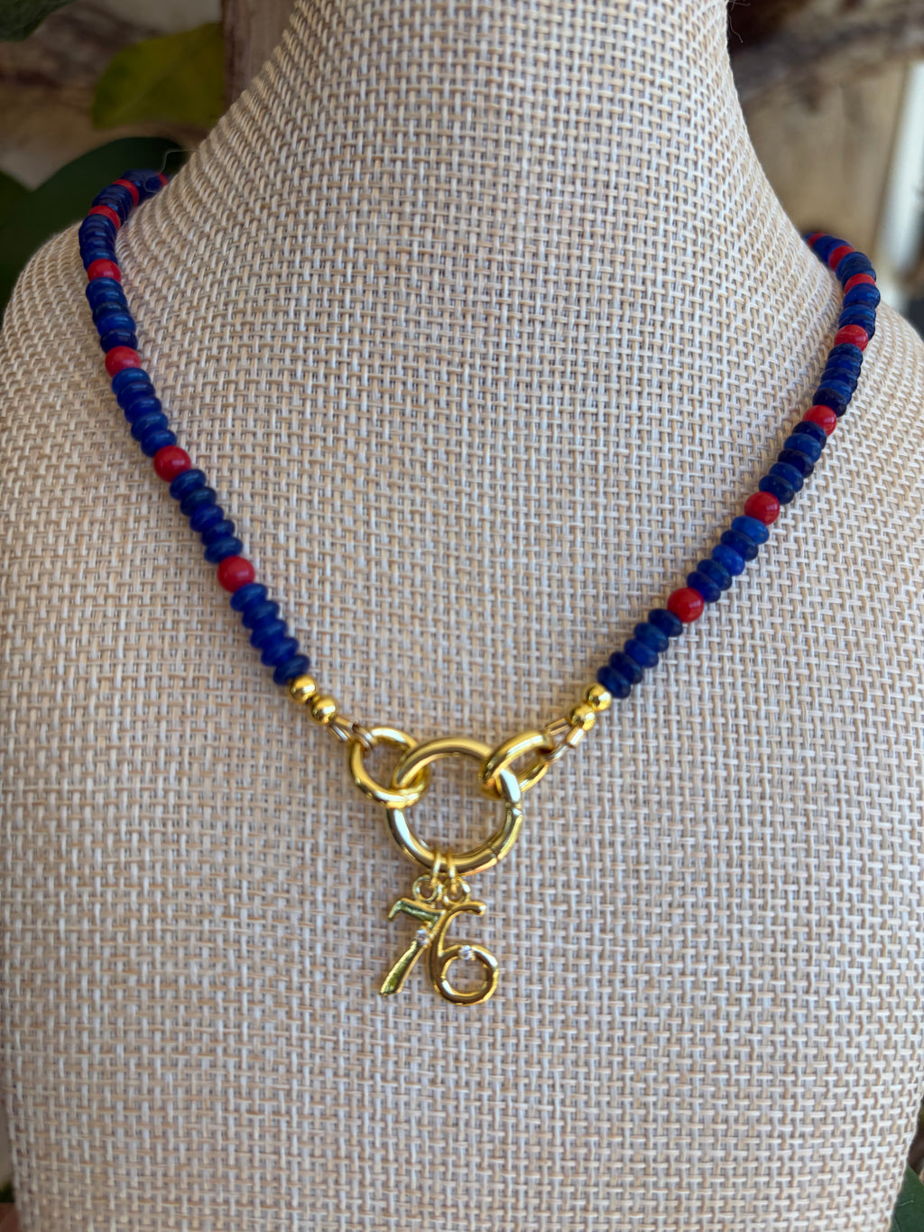 Close up of blue and red seed bead necklace with gold 76 charm