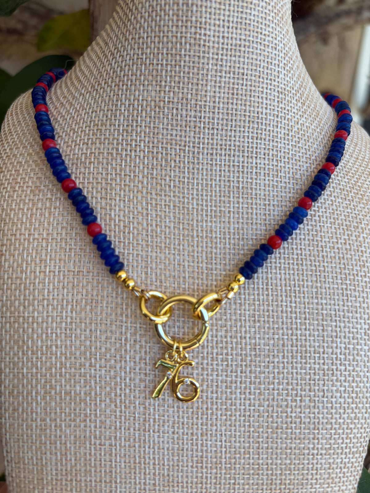 Close up of blue and red seed bead necklace with gold 76 charm