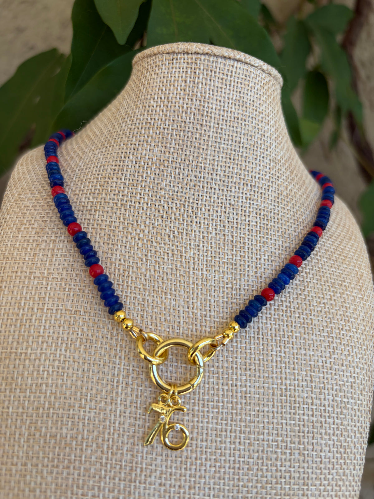 Blue and red seed bead necklace with gold 76 charm on mannequin