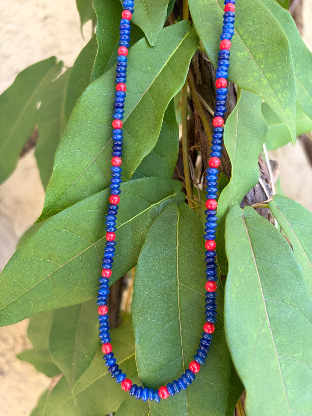 Blue and red seed bead necklace draped on leaves