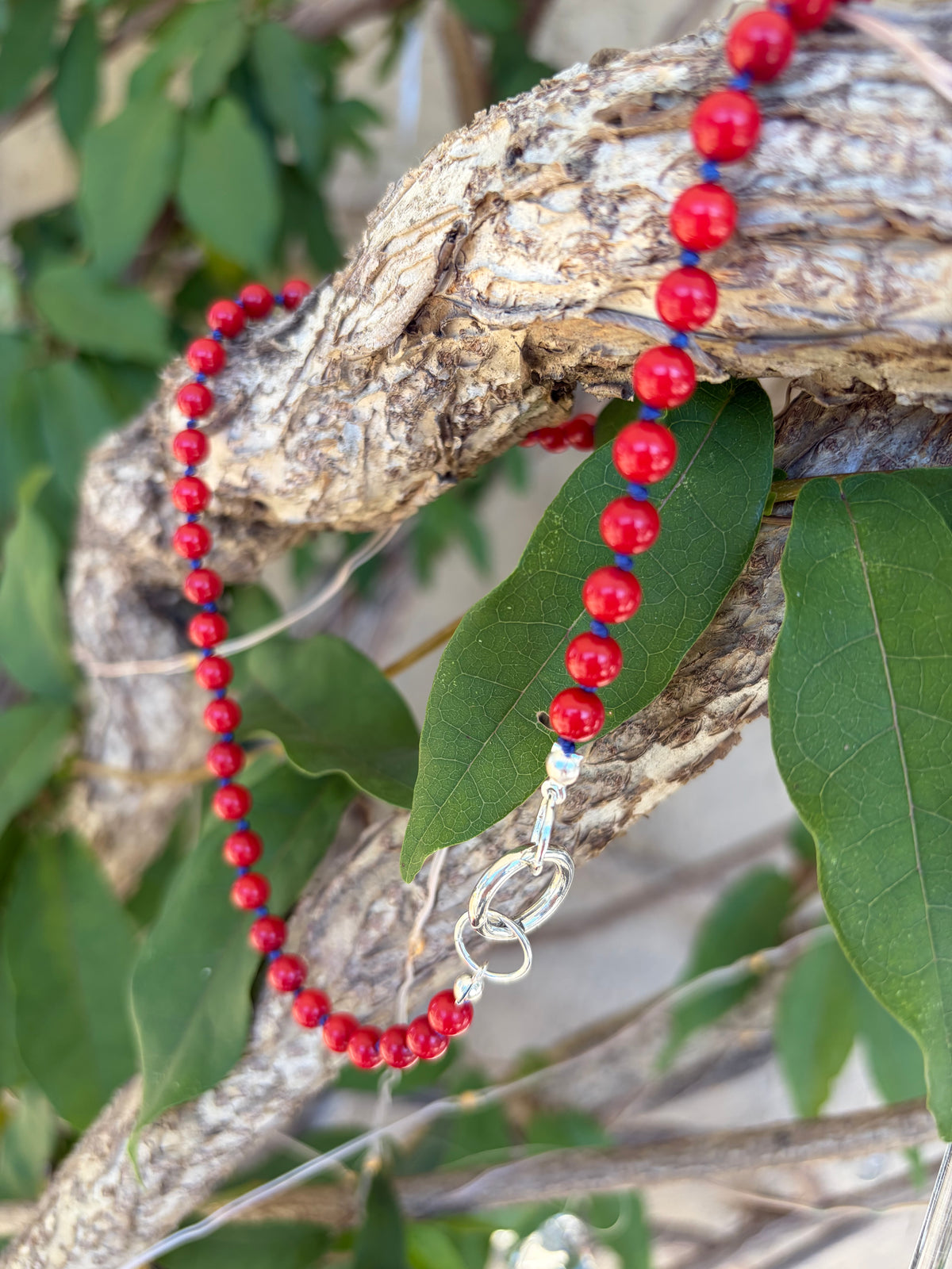 Red beaded necklace with sterling silver clasp on driftwood